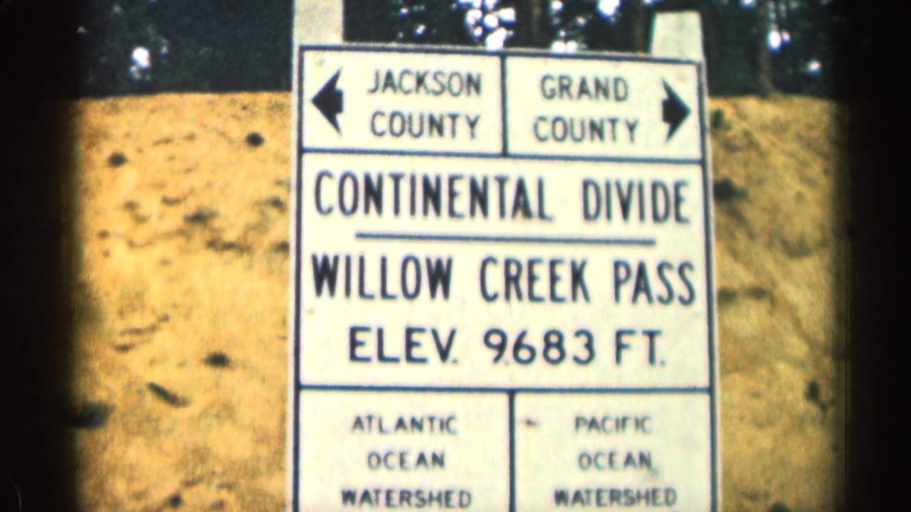 1963 Colorado 8mm frame showing the Willow Creek Pass Continental Divide sign with Jackson and Grand County arrows and elevation at 9,683 feet.