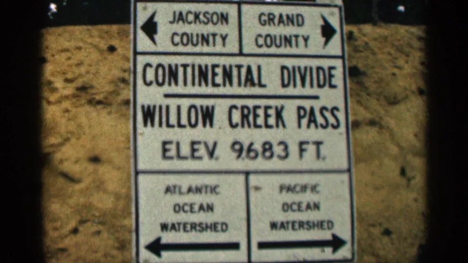 1963 Colorado home-movie still tightly frames the Willow Creek Pass Continental Divide sign and its elevation marking.