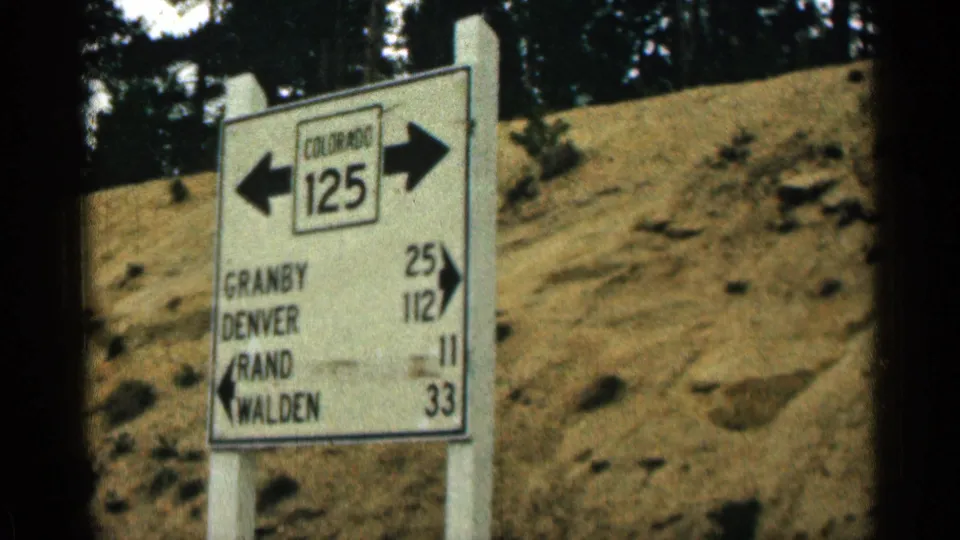 1963 Colorado roadside frame showing a Colorado 125 directional sign with arrows and distances to Granby, Denver, Rand, and Walden.