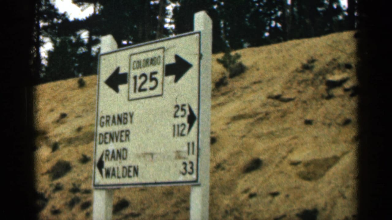 Colorado 125 roadside sign with arrows and destination mileage beside a dry embankment.
