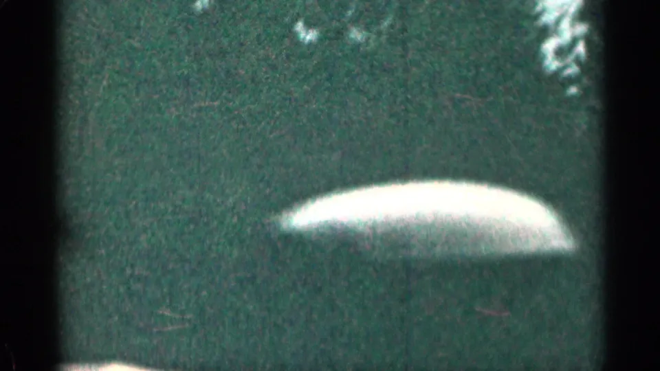 1963 Colorado home-movie frame showing trees and grass through the passenger window, with a pale car interior or door edge in the foreground.
