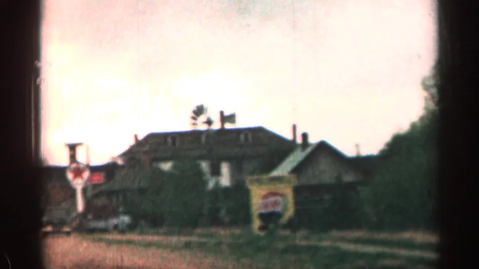 1963 Colorado 8mm frame showing a rustic roadside building, vintage parked cars, signs, and a small windmill silhouette.
