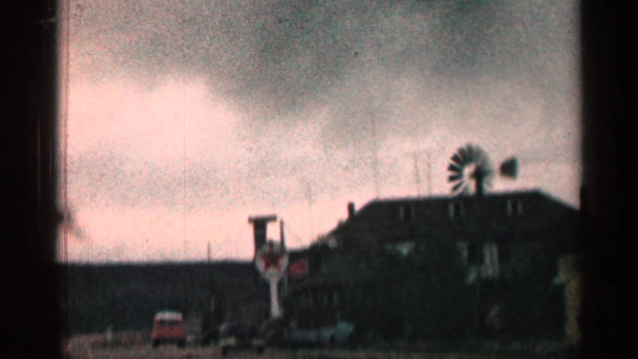 1963 Colorado 8mm frame showing a roadside stop with a low building, red and white sign, classic cars, and cloudy sky.