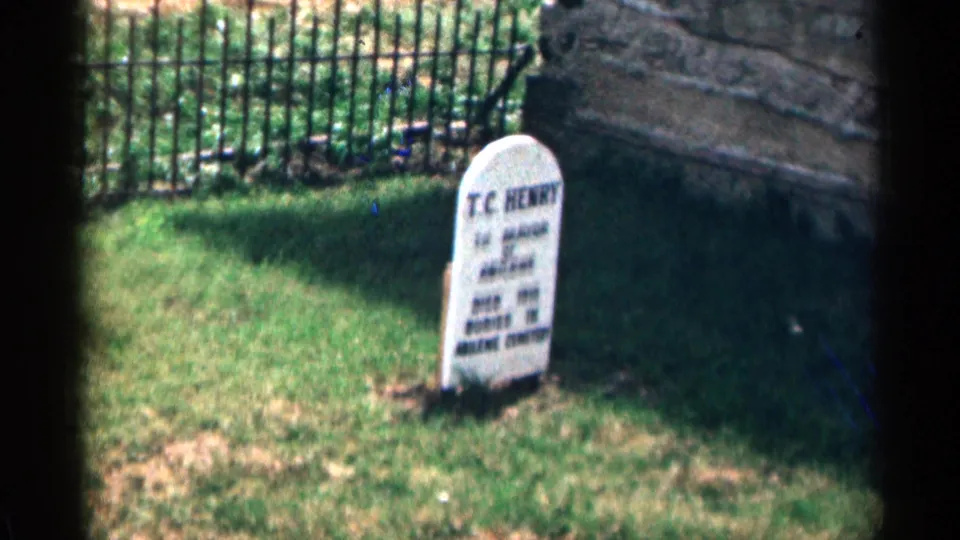 1963 8mm Colorado cemetery shot with the T.C. Henry headstone angled in the foreground and iron fencing behind it.