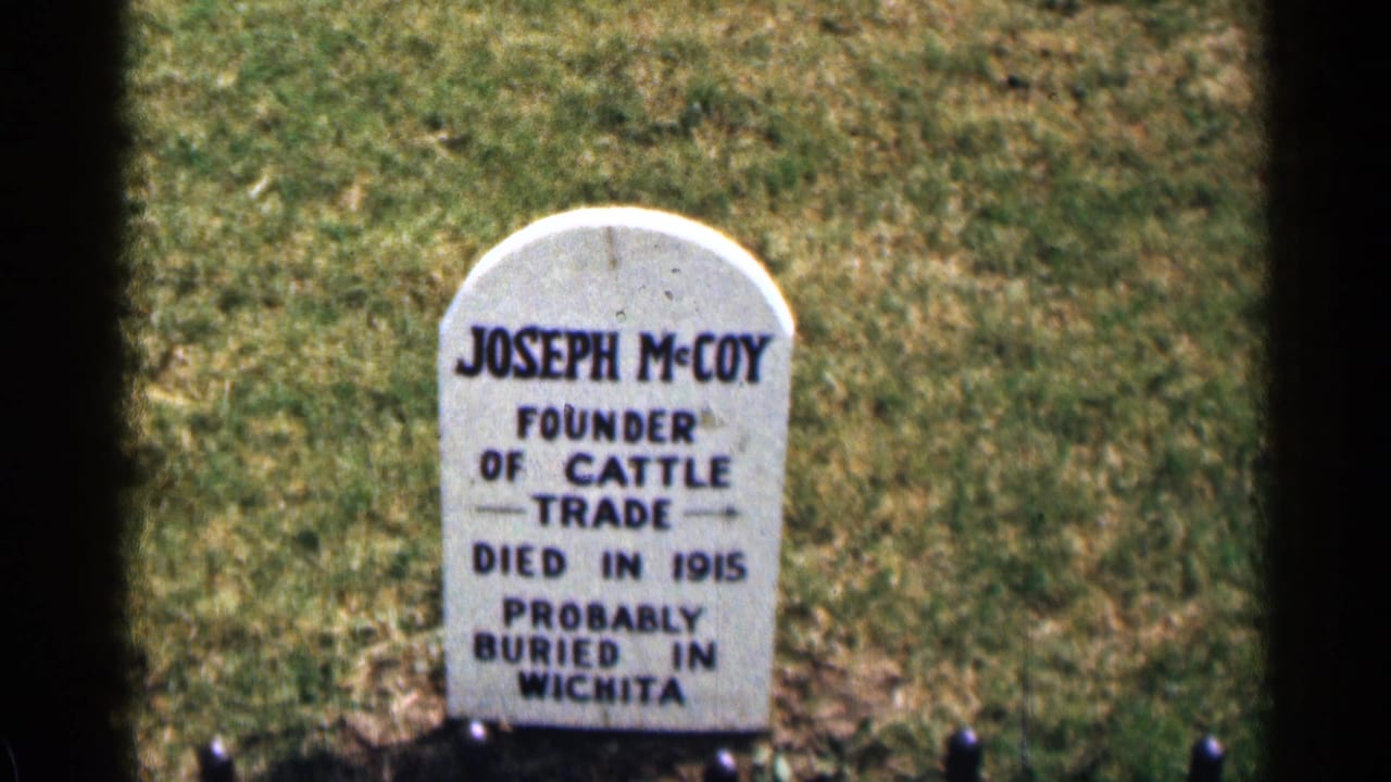 Colorado 1963 8mm frame showing a white Joseph McCoy marker in a grassy area, with dark film-edge shadow at left.