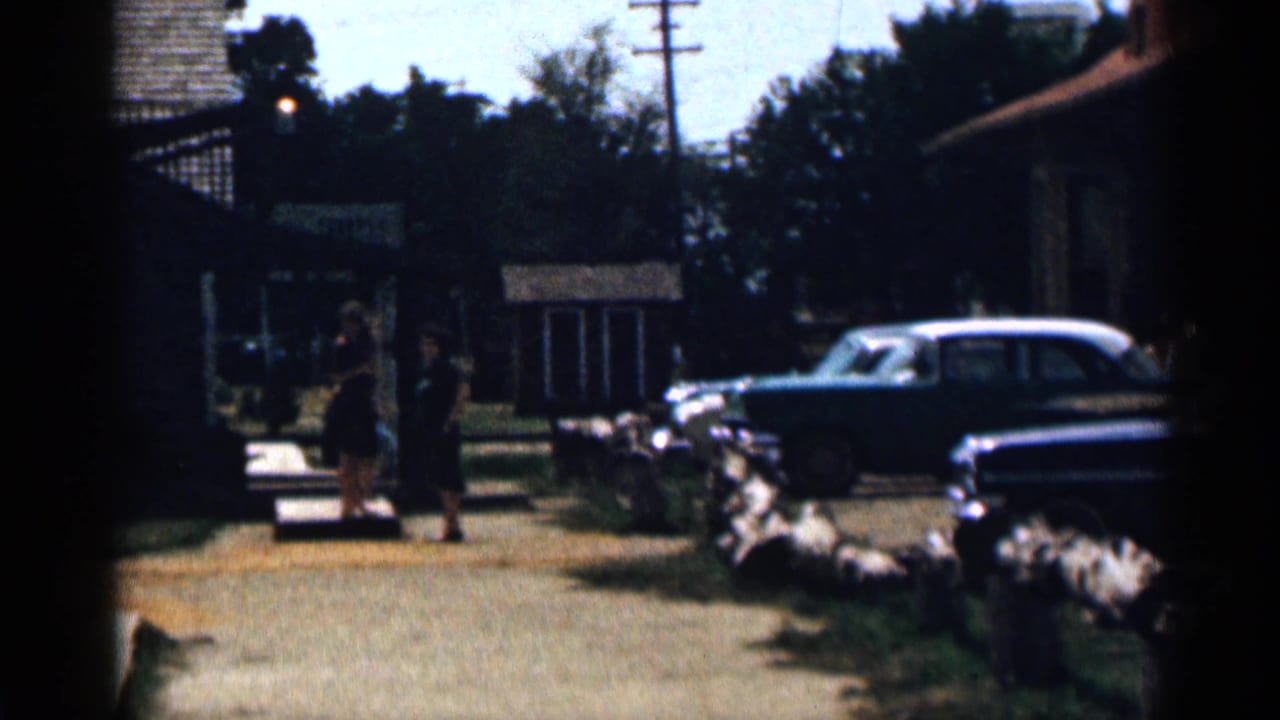 Residential street with parked cars and two women near a sidewalk.
