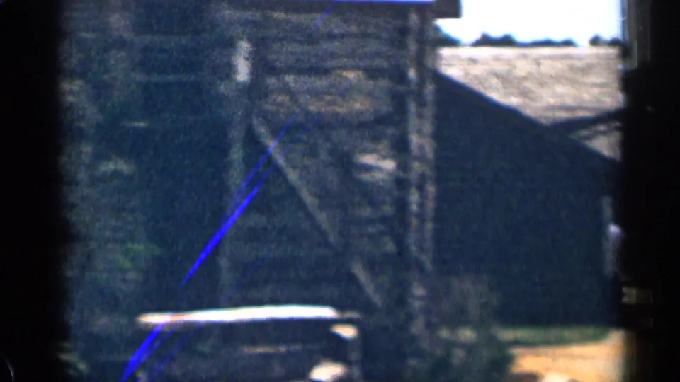 Colorado 1963 frame showing a rustic wooden shed or barn, shadowed foreground, and the roofline of a parked car.