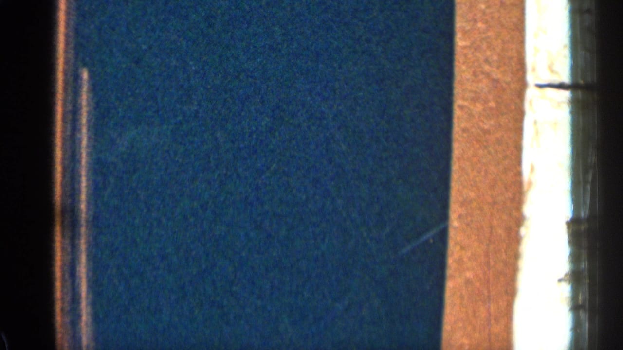 1963 Colorado 8mm frame showing a dim blue interior wall, a bright window edge, warm trim, and heavy film grain.