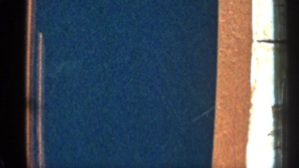 1963 Colorado 8mm frame showing a dim blue interior wall, a bright window edge, warm trim, and heavy film grain.
