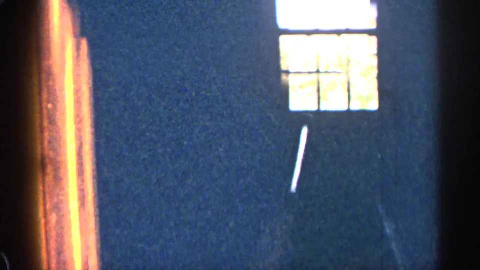 1963 Colorado 8mm still showing a bright divided window, deep blue wall, warm side trim, and a white diagonal streak.