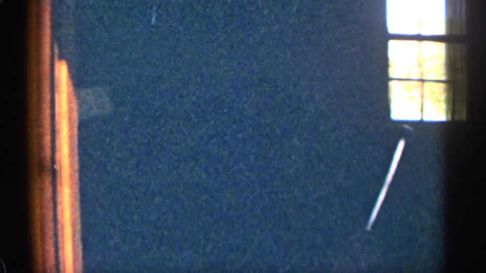 1963 Colorado home-movie frame showing a bright window, dark blue interior wall, warm trim, and visible 8mm grain.