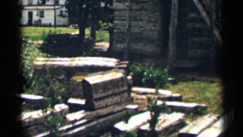 1963 Colorado yard scene with stone remnants, white planks, trees, lawn, and a small house visible in the background.