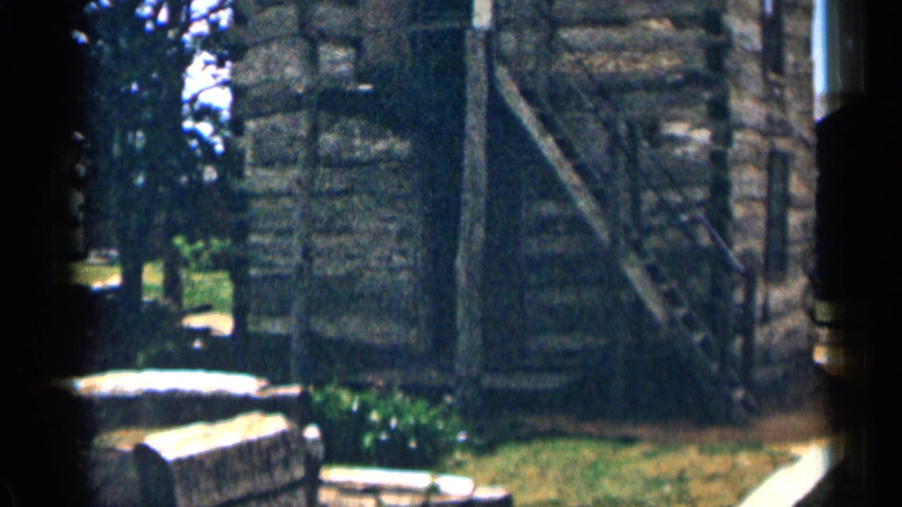 Rustic log cabin exterior with stairs, grass, trees, and bright sky.