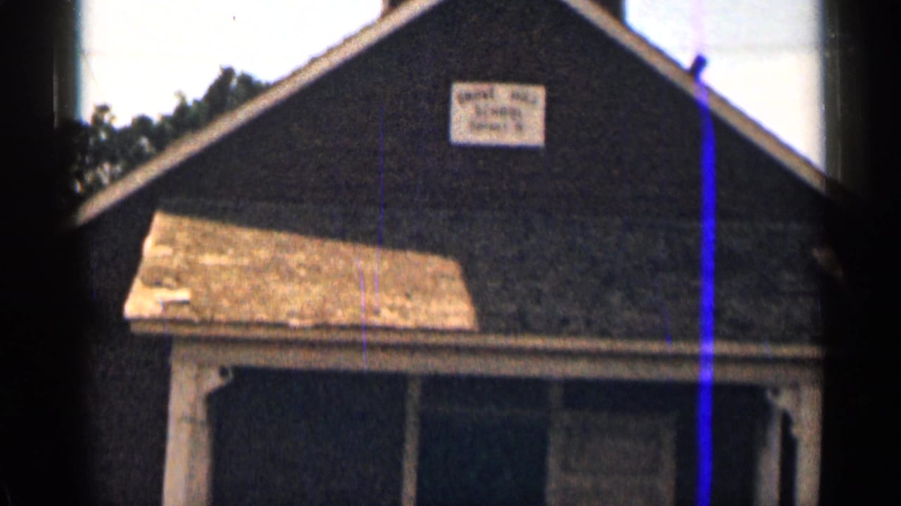 Weathered dark-sided house with a porch and faded sign above the entrance.