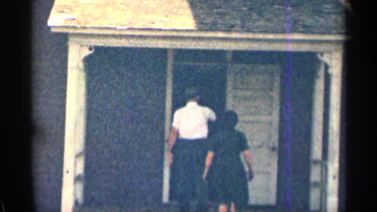 Man and woman walking toward the doorway of the weathered house.