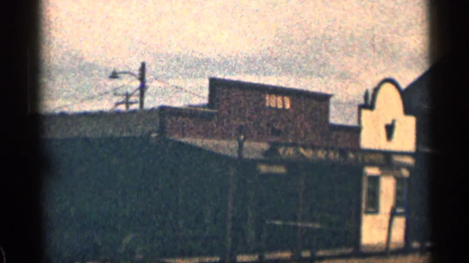1963 Colorado 8mm frame of a weathered wooden street-side building with roofline signage, a small front form, pale sky, and deep shadows.