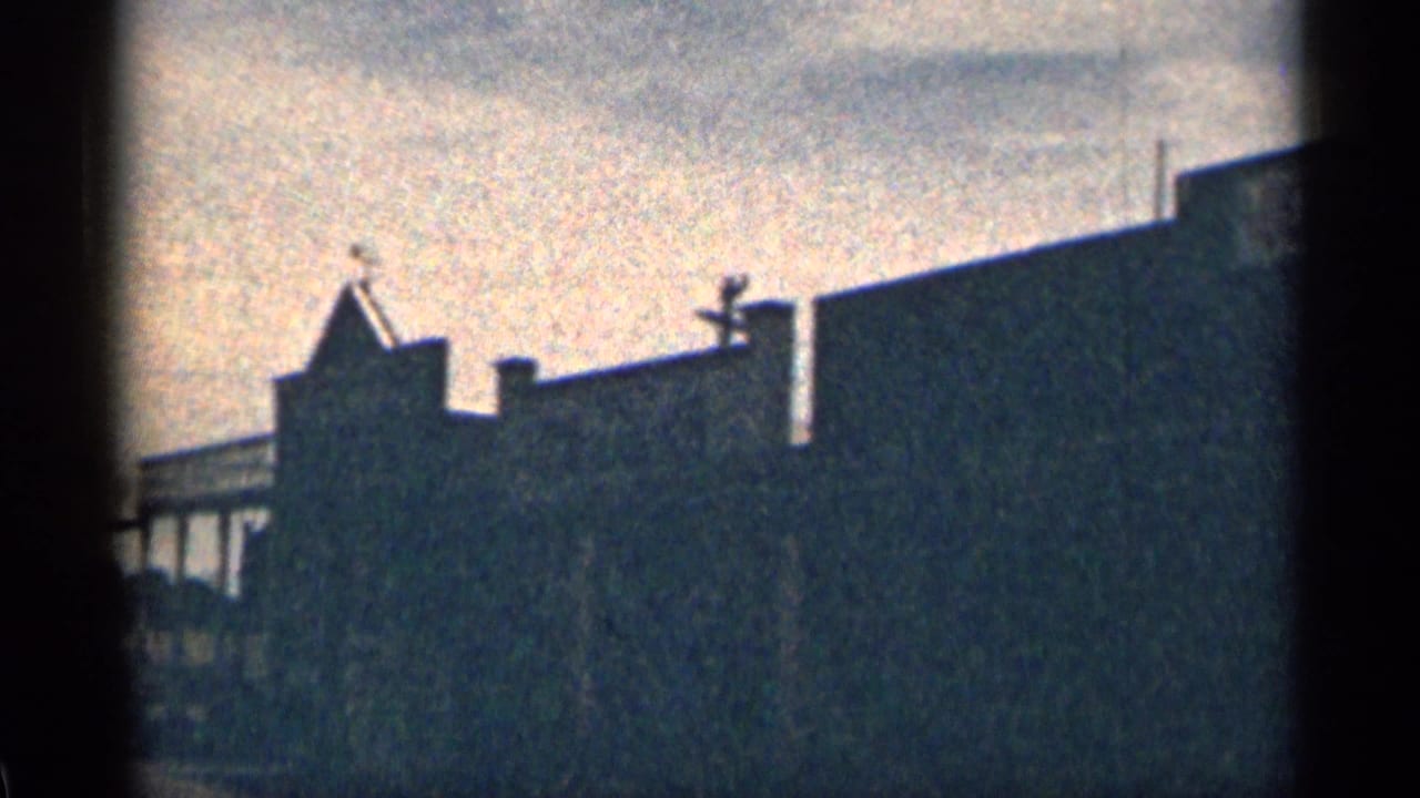 1963 Colorado 8mm frame showing backlit Western-style rooflines and dark building facades under a hazy sky.