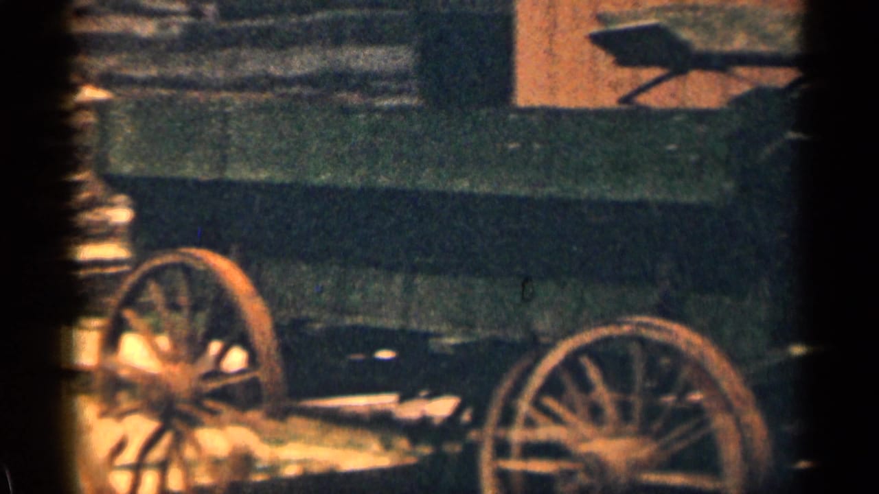 Wooden wagon with large spoked wheels beside a log wall.