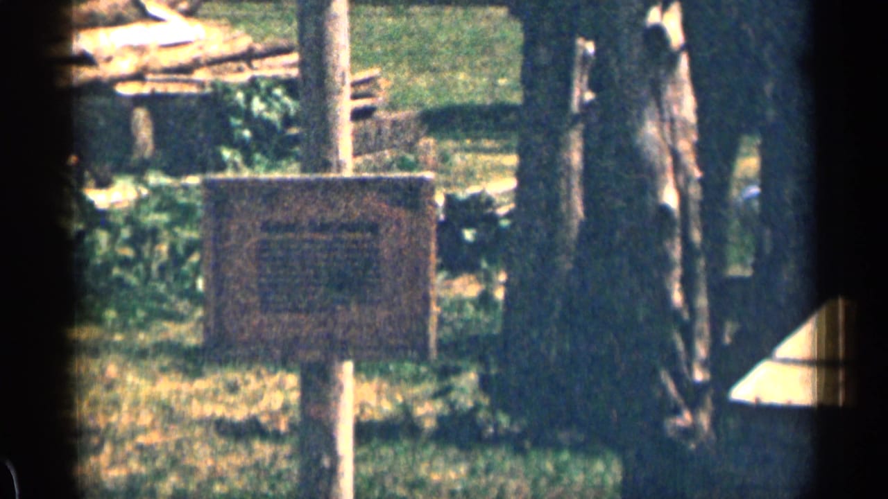 1963 Colorado home-movie frame showing rural grounds near a landmark area, with a signboard, fence posts, trees, and heavy film edge shadow.