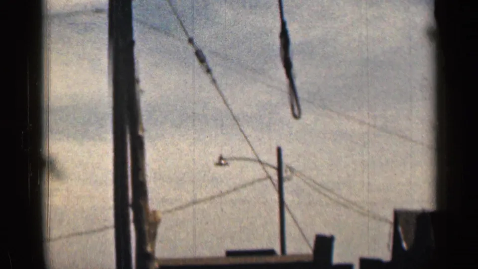 1963 Colorado home-movie frame looking past a dark foreground edge toward utility poles, wires, cloudy sky, and part of a hanging rope or noose.