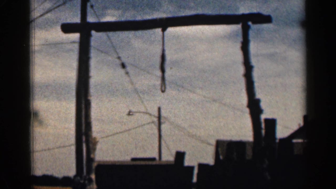 1963 Colorado 8mm view of a wooden gallows and hanging noose, framed above dark outdoor structures and power lines.