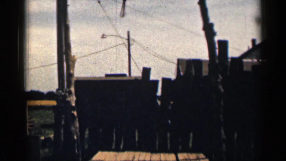 1963 Colorado 8mm frame showing the lower gallows area with dark fence sections, grass, and part of a plank platform.