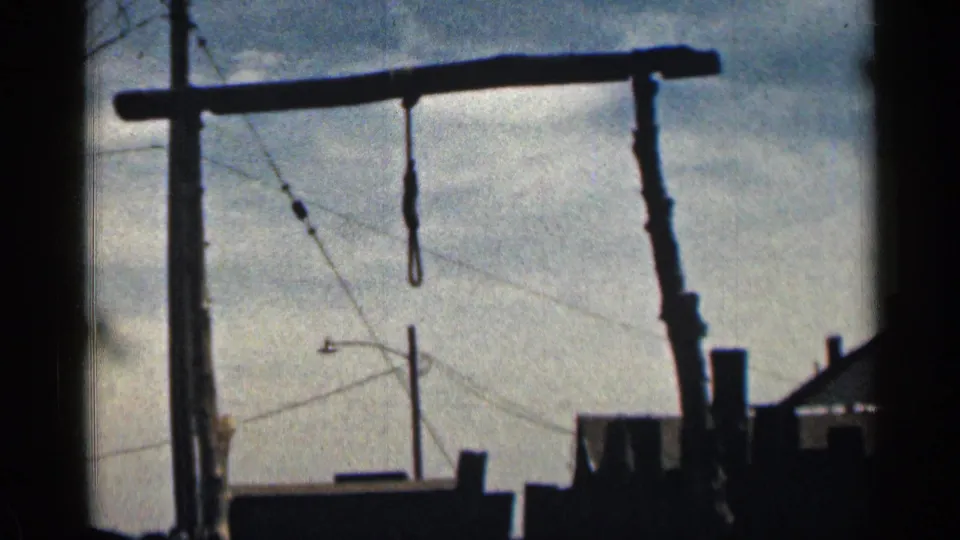 1963 Colorado 8mm frame showing a gallows-like timber frame with a hanging loop, utility wires, sky, and a partial roofline.