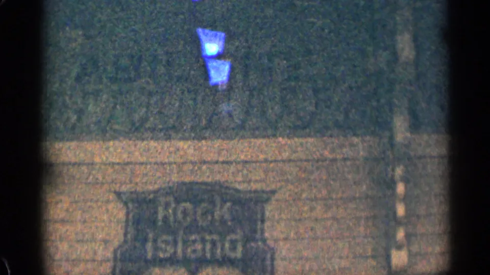 Close 8mm view of a weathered Rock Island sign mounted on a brick wall, with a blue light visible above the sign.