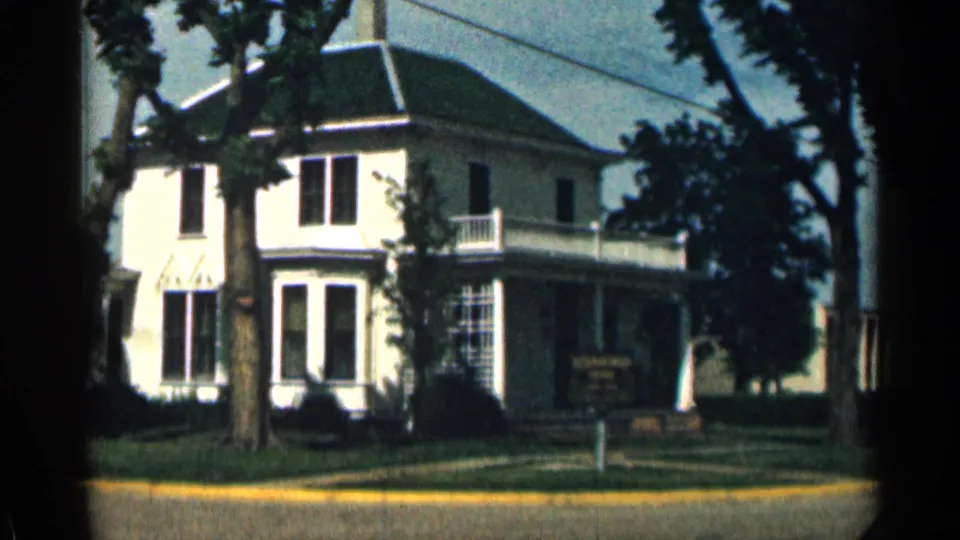 Final 1963 Colorado frame showing the house exterior, shaded porch area, sign, tree-lined frontage, and yellow curb.