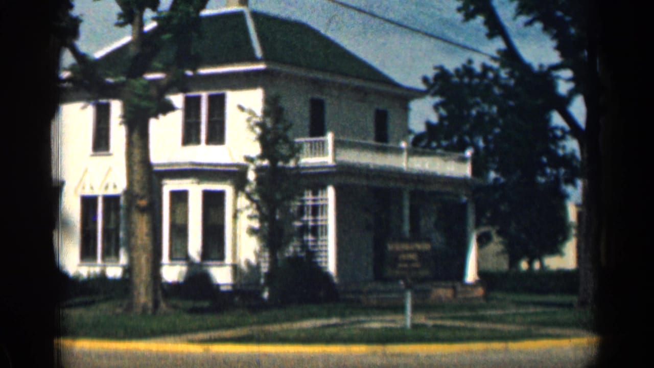 1963 Colorado 8mm frame showing the Eisenhower Home exterior, with a white facade, green roof, balcony, porch, trees, lawn, and sign.