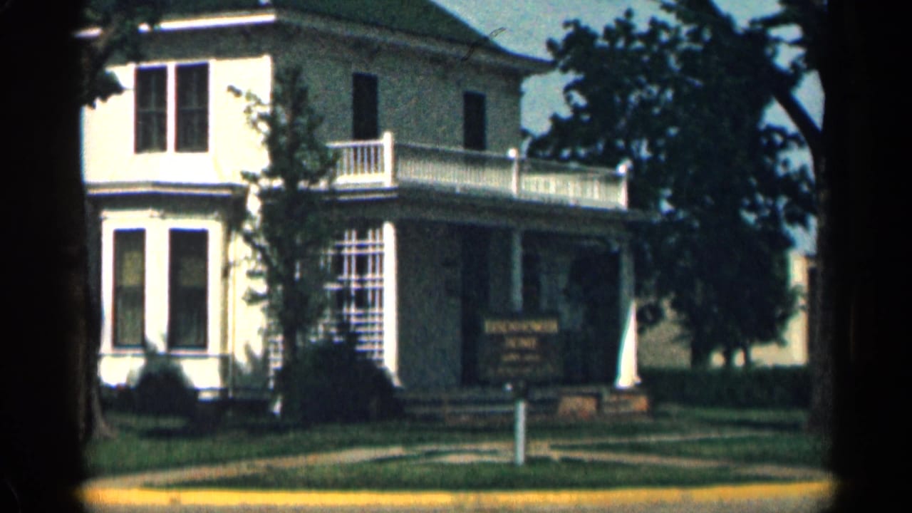 1963 Colorado 8mm view of the Eisenhower Home, centered on the porch, balcony railing, windows, lawn, trees, and sign.