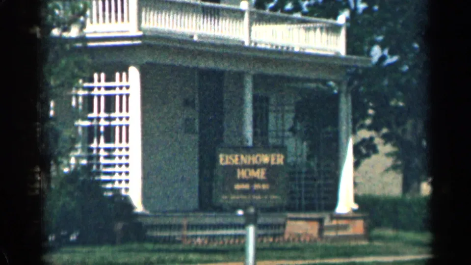 Tight 1963 Colorado 8mm frame emphasizing the Eisenhower Home porch sign, balcony railing, white columns, window lattice, and shaded lawn.