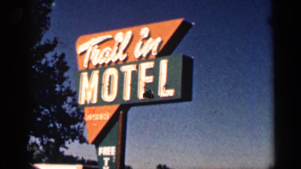 1963 Colorado 8mm frame showing the Trail In Motel neon roadside sign, with tree silhouettes and twilight sky behind it.