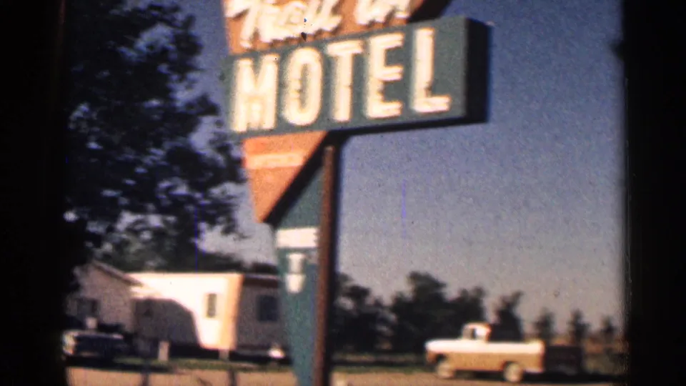 1963 Colorado 8mm frame of the Trail In Motel sign beside a white pickup truck, mobile home, trees, and open roadside ground.