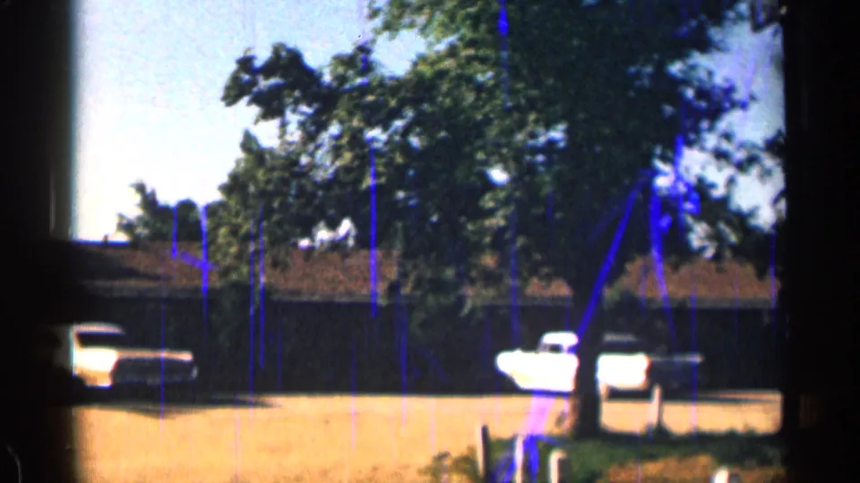 1963 Colorado motel-lot frame showing a white pickup, trees, utility poles, and low buildings with visible 8mm film wear.