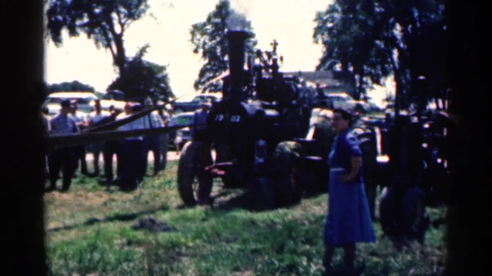 Outdoor Montgomery gathering in 1963 with spectators on grass near a black steam engine and a woman in a blue dress in front.