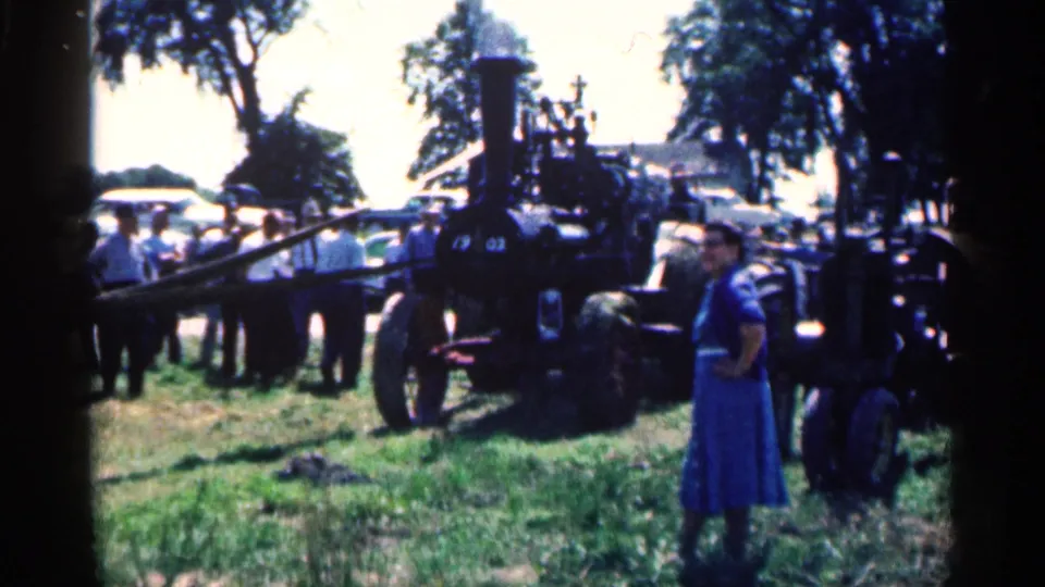 Woman in a blue dress stands in the foreground as a crowd looks over a black steam engine at a 1963 Montgomery outdoor gathering.