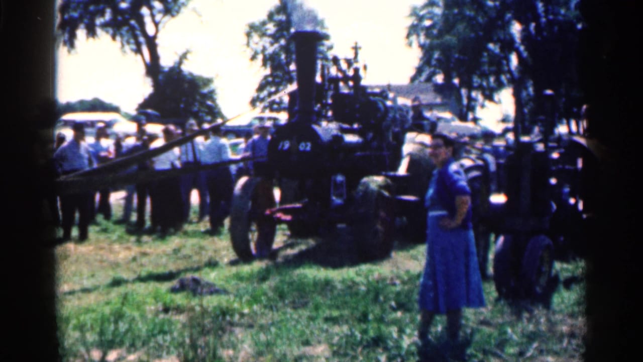 Steam traction engine on a grassy field with visitors gathered nearby.
