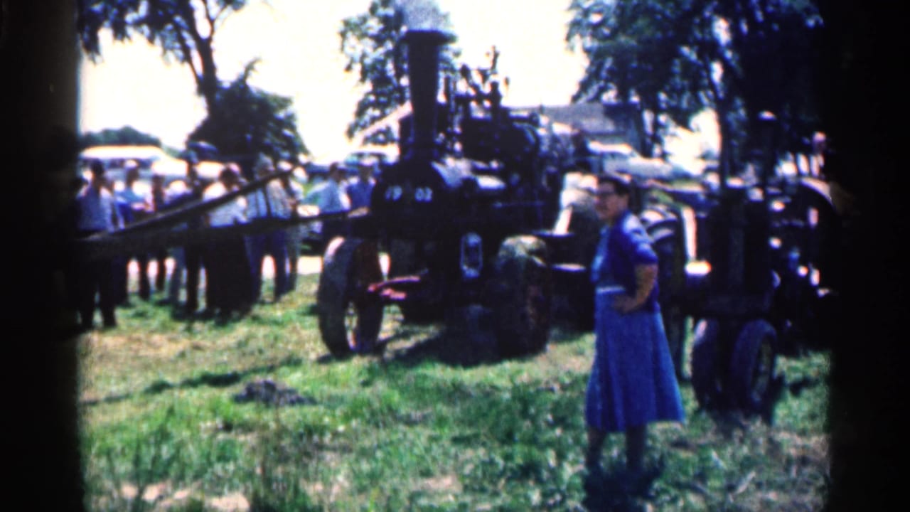Crowd standing around a black steam engine in an open field.