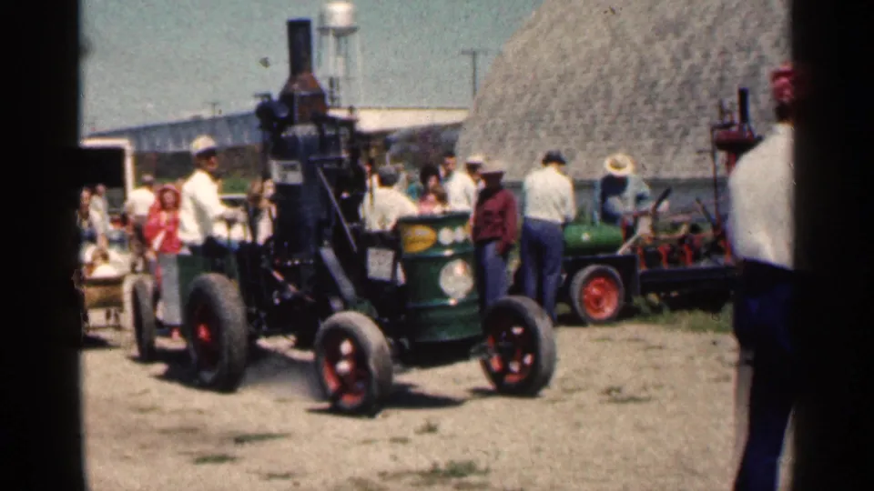 1963 Montgomery, Minnesota frame showing a vintage tractor in front of spectators, haystack, farm equipment, and distant buildings.