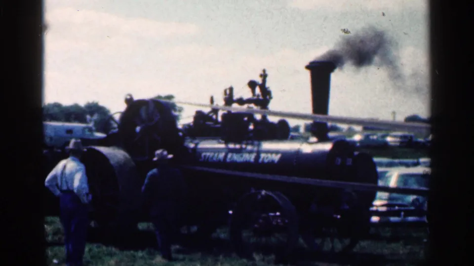 The larger steam engine remains in view at the 1963 Montgomery, Minnesota event, with smoke from the stack and people standing near the side lettering.