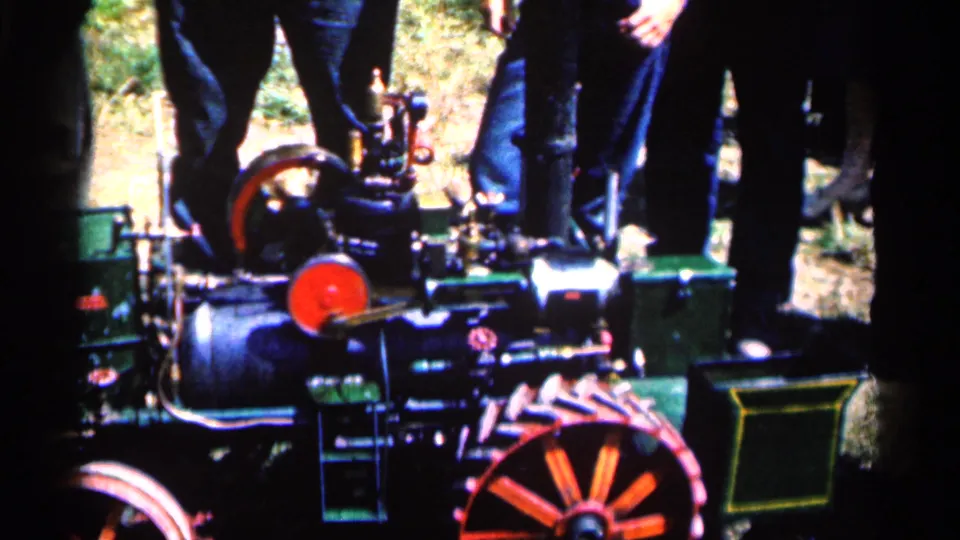Close frame from the Montgomery steam engine display, showing red spokes, dark boiler parts, green panels, and onlookers partly cropped by the camera.