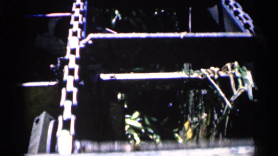 A shadowed 1963 industrial corn processing view in Montgomery, Minnesota, with chain sections, metal frames, and green husks visible inside the machinery.