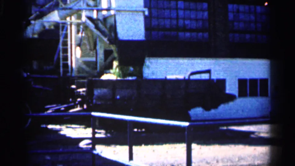 1963 Montgomery, Minnesota home-movie frame showing shadowed machinery, a ladder, and a farm building exterior.