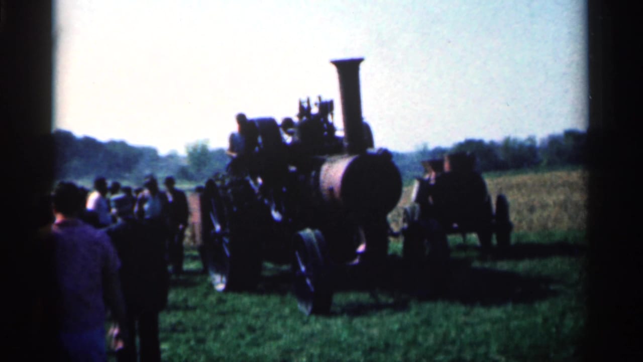 Crowd gathers around a steam tractor in a grassy field.