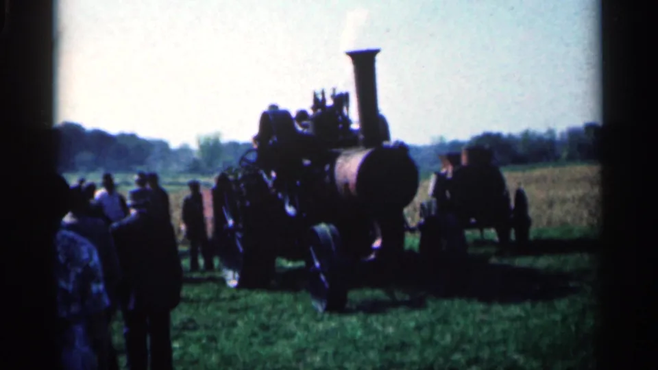 A group watches a steam tractor in a grassy Montgomery, Minnesota field, with the tall smokestack and front boiler prominent.