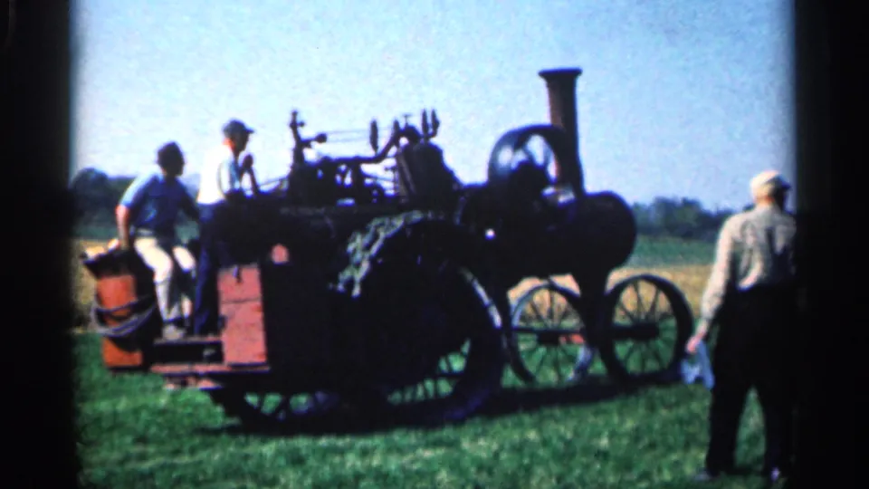 Side view of the 1963 Montgomery, Minnesota steam tractor display, with men nearby and the tractor's wheel, platform, and smokestack visible.