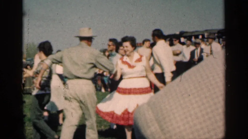 At an outdoor Montgomery, Minnesota gathering in 1963, adults in hats and dresses dance on grass with onlookers nearby.