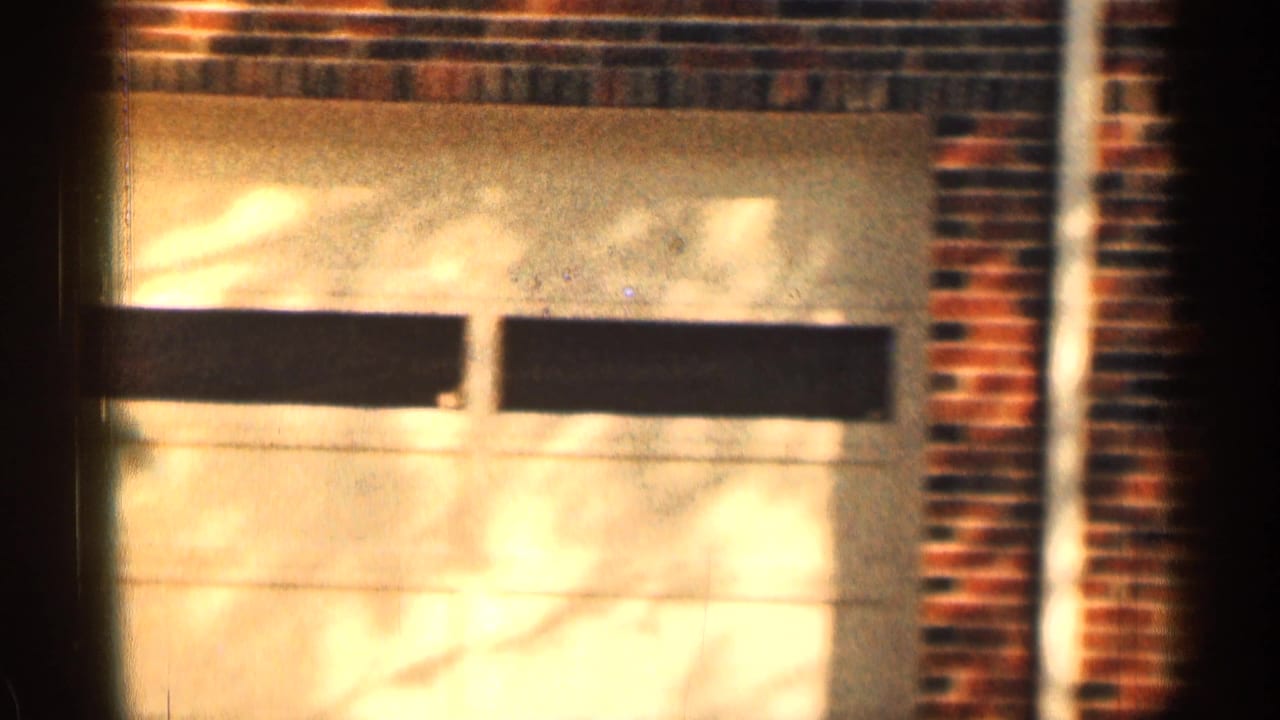 1963 Texas 8mm frame showing a brick residential garage facade with a pale garage door and sunlit shadows.