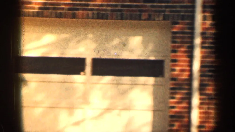 1963 Texas 8mm frame showing a brick residential garage facade with a pale garage door and sunlit shadows.